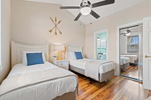 Ein Schlafzimmer mit zwei Betten, einem Deckenventilator, einem Nachttisch mit Lampe und einer Tür zu einem Badezimmer.