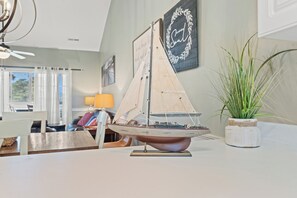 Ein Modellsegelboot auf einem Tisch, eine Topfpflanze und eine Wand mit einem gerahmten Zitat.
