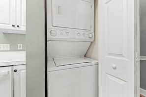 A laundry room with a stacked washer and dryer, a door, and a wall-mounted electrical outlet. - Peaceful Point | Golf Course Views (Myrtle Beach)
