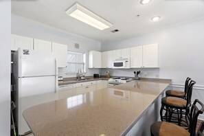 A modern kitchen with white cabinetry, a large island, a microwave, and a stove. - On Holiday | Pool Views + Private Balcony (Myrtle Beach)