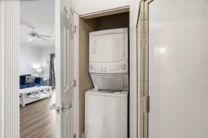 Une buanderie équipée d’un lave-linge et d’un sèche-linge à chargement frontal, d’un ventilateur de plafond et d’un canapé bleu dans le salon attenant.