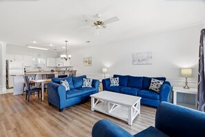 Una sala de estar moderna con un sofá azul, una mesa de centro blanca y un ventilador de techo.