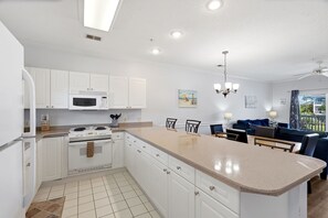 A modern kitchen with white cabinetry, a central island, and a dining area with a blue sofa.