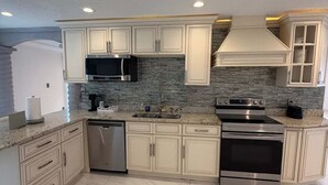 A modern kitchen with white cabinets, a granite countertop, a stainless steel range hood, and a built-in oven. - The Marble Manor | House & Loft (Myrtle Beach)
