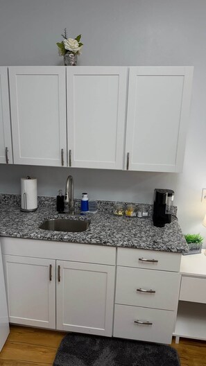 Eine Küche mit weißen Schränken, einer Granitabdeckung, einem Spülbecken, einer Kaffeemaschine und einem kleinen Topfpflanzen.