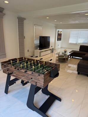 Uma sala de estar com mesa de futebol, televisão e sofá.