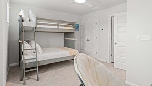 Une chambre avec un lit superposé, un ventilateur de plafond, des murs blancs et une porte.