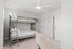 Ein Schlafraum mit Etagenbetten, Deckenventilator, weißen Wänden und einer Tür.