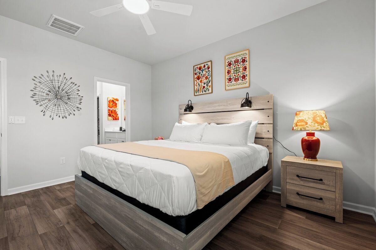 Una camera da letto con un letto, comodini, una ventola a soffitto, opere d'arte e una lampada.