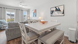 Un espace repas avec une table blanche, des chaises rembourrées et des œuvres d’art accrochées aux murs.