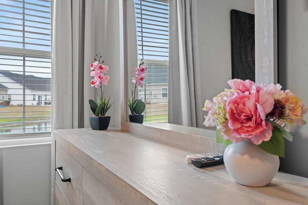 A room with a window, a vase with flowers, and a remote control on the windowsill.