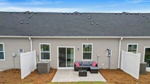 Un immeuble résidentiel à l’extérieur gris, doté d’un patio couvert avec un canapé d’angle gris et une petite table, et un ciel dégagé.