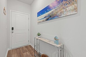 Un passadís amb una porta blanca, una taula de consola de marbre amb una planta i un objecte blau amb forma de casa, i un quadre gran d'un paisatge nevado.