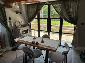 A dining area with a table, chairs, and a view of a garden through large windows. - THE LOST RADISH - Cosy and romantic Cotswold cottage with private garden (Kingham)