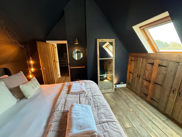 A bedroom with a large bed, wooden wardrobe, and a skylight. - THE LOST RADISH - Cosy and romantic Cotswold cottage with private garden (Kingham)
