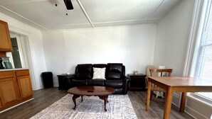 Ein Wohnzimmer mit einer schwarzen Ledersofa, einem Holztisch und einem Esstisch mit Stühlen.