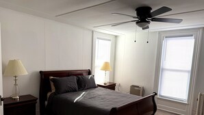 Ein Schlafzimmer mit einem Bett, zwei Nachttischen, einem Deckenventilator und einem Fenster mit Jalousien.