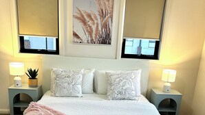 Een slaapkamer met een bed, twee nachtkastjes, een raam en een kunstwerk aan de muur.