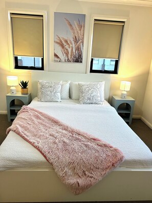Une chambre à coucher comprenant un lit, deux tables de chevet, une fenêtre et une œuvre d’art accrochée au mur.