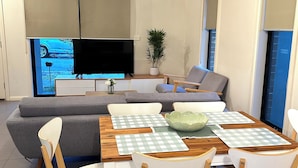 Een moderne woonkamer met een houten eettafel, witte stoelen, een grijze bank en een flatscreen-televisie.