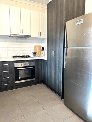 A modern kitchen with white cabinets, a stainless steel refrigerator, a built-in oven, and a gas stove. - Cozy Retreat@Melbourne Airport (Craigieburn)