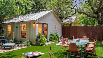 A small white shed with a door, a table with chairs, and a target game on the grass.
