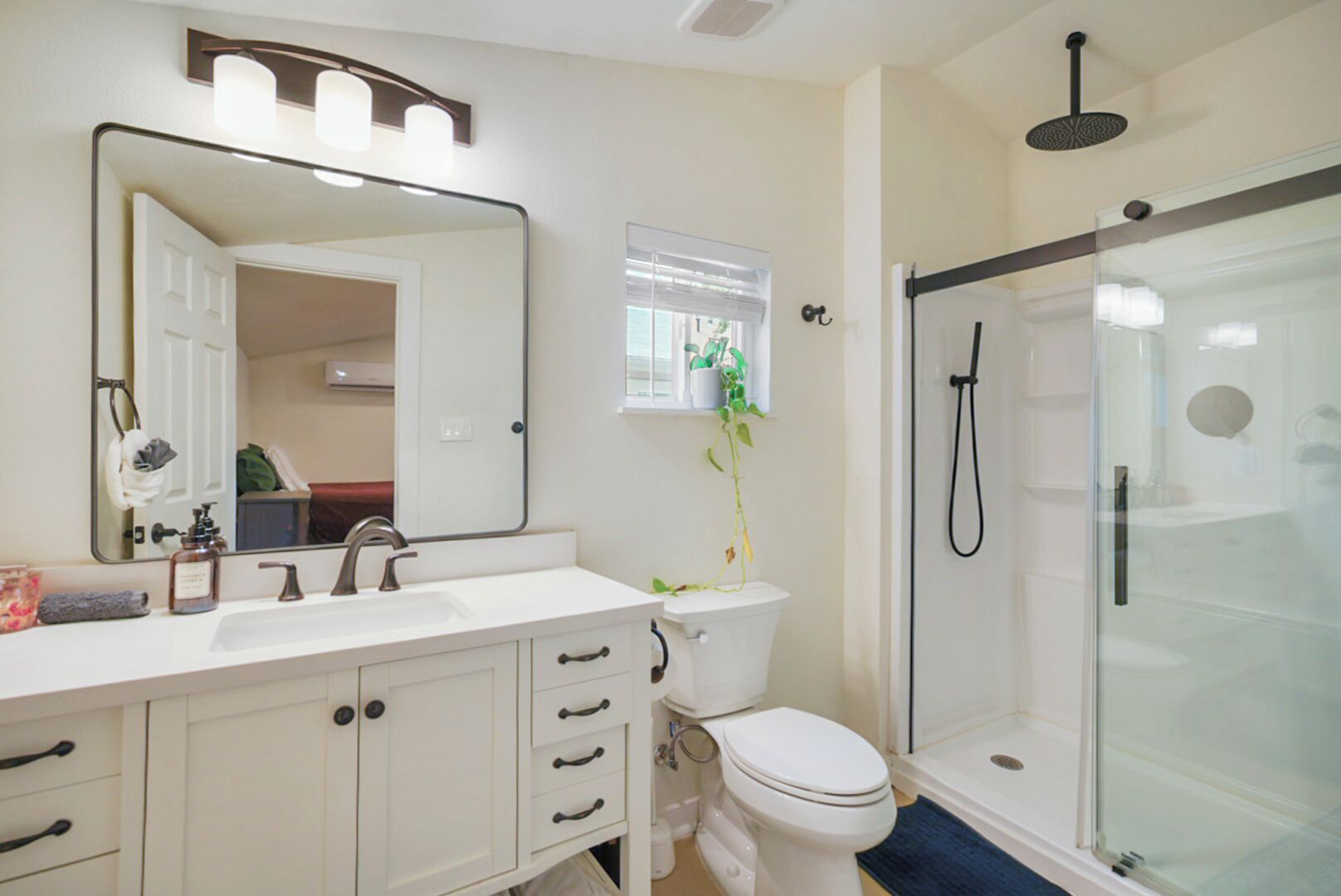 A bathroom with a white vanity, a large mirror, a toilet, and a glass-enclosed shower.