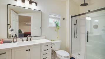 A bathroom with a white vanity, a large mirror, a toilet, and a glass-enclosed shower.