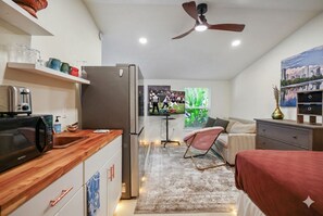 Ein kompakter Wohnraum mit Küchenzeile, Deckenventilator, Fernseher und Bett.