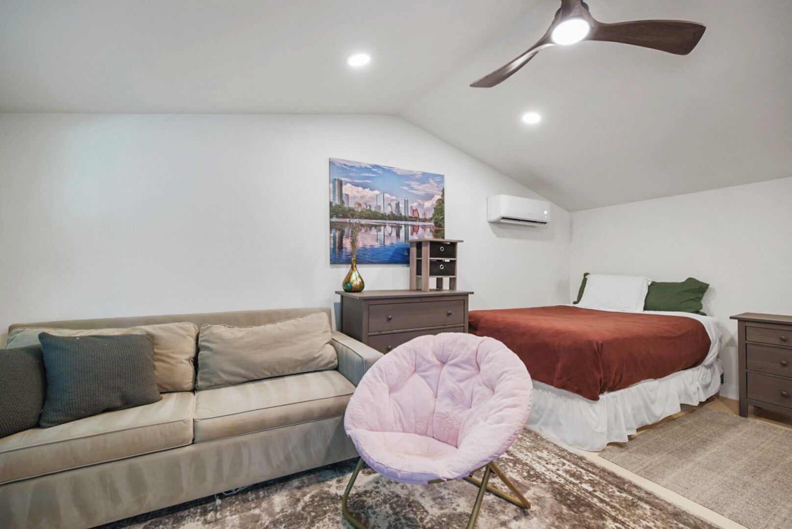 Une chambre à coucher avec un lit, un canapé, une chaise, un ventilateur de plafond et un tableau accroché au mur.