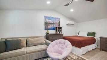 Une chambre à coucher avec un lit, un canapé, une chaise, un ventilateur de plafond et un tableau accroché au mur.