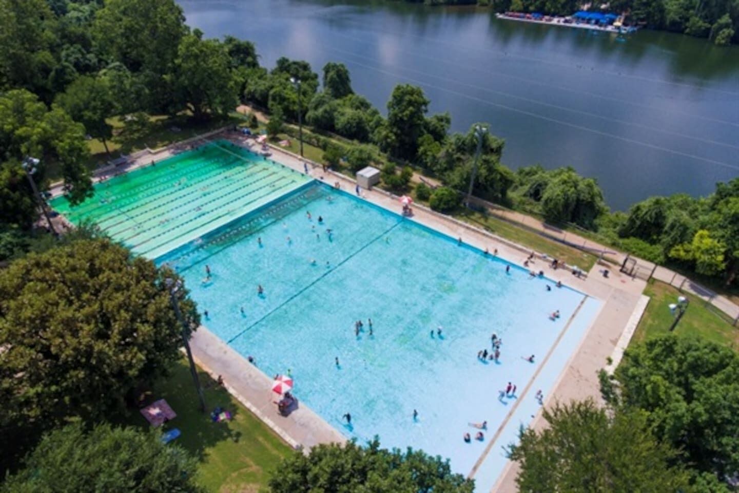Ein Luftbild eines rechteckigen Schwimmbeckens, umgeben von Bäumen und einem Gewässer.