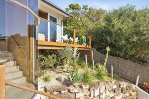 Ein modernes Haus mit einer Glasstufenanlage, Sitzgelegenheiten im Freien und einem Garten mit Kakteen und anderen Pflanzen.