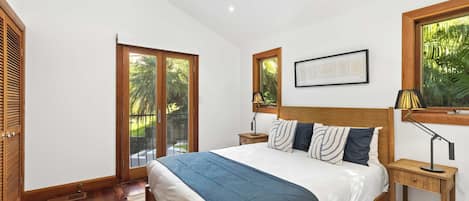 Een slaapkamer met een bed, een houten hoofdbord, nachtkastjes, een raam met uitzicht op groen en een ingelijste foto aan de muur.