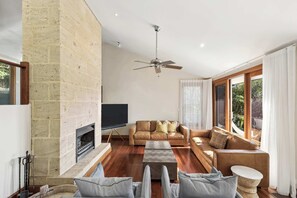Ein Wohnzimmer mit Kamin, einer Couch, einem Fernseher und einem Deckenventilator.