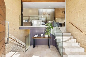 Uma escadaria moderna com guarda-corrimão de vidro, um banco de madeira com objetos decorativos e vista para um quarto com parede de pedra e um quadro emoldurado.
