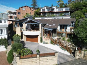 A modern two-story house with a covered patio, a stone staircase, and a landscaped garden. - Avoca Village. 150m to Beach. Sleeps 10 (Avoca Beach)