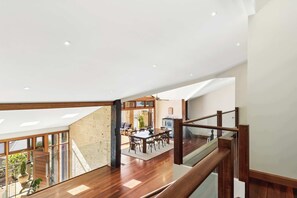 A spacious interior with a high ceiling, wooden flooring, and a dining area with a large table and chairs. - Avoca Village. 150m to Beach. Sleeps 10 (Avoca Beach)