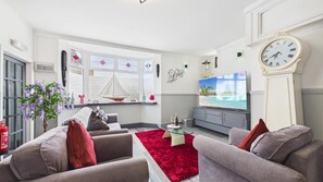 En stue med tv, sofa, rød måtte og en sejlbådsdekoration.
