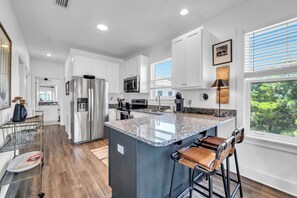 A modern kitchen with white cabinets, stainless steel appliances, a granite countertop island, and a view of greenery outside. - Hidden Lake Condos 131, walk to Gulf Place! (Santa Rosa Beach)