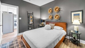 Ein Schlafzimmer mit einem Bett, einem Nachttisch, einer Lampe, einem Wandbild und einem Deckenventilator.