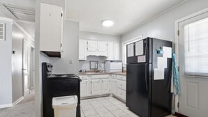 Una cocina con armarios blancos, estufa negra, refrigerador negro y un bote de basura.
