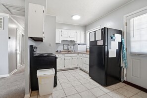 A kitchen with white cabinets, a black stove, a black refrigerator, and a trash bin. - Beautiful 3-bedroom house (Dayton)