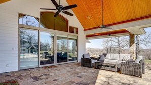A covered patio with stone flooring, wicker furniture, and a ceiling fan. - Post Oak Estate - Pool, Barn, 2 Guest Homes, 16 Ac (Cleburne)