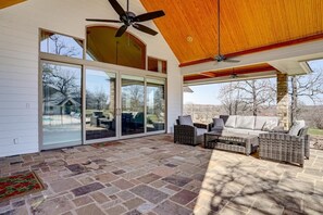 A covered patio with stone flooring, wicker furniture, and a ceiling fan. - Post Oak Estate - Pool, Barn, 2 Guest Homes, 16 Ac (Cleburne)