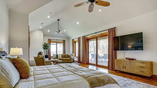 A spacious bedroom with a large bed, a ceiling fan, a TV, and a sliding glass door to a balcony. - Post Oak Estate - Pool, Barn, 2 Guest Homes, 16 Ac (Cleburne)