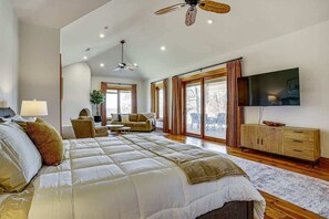 Amplia habitación con una cama grande, ventilador de techo, televisor y puerta corrediza de vidrio a un balcón.