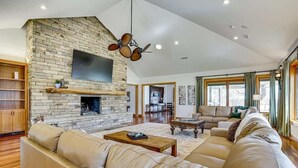A spacious living room with a stone fireplace, leather sofas, and a flat-screen TV mounted on the wall. - Post Oak Estate - Pool, Barn, 2 Guest Homes, 16 Ac (Cleburne)