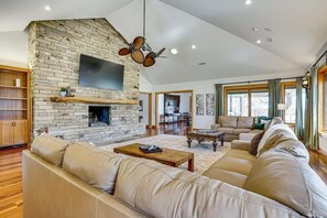 A spacious living room with a stone fireplace, leather sofas, and a flat-screen TV mounted on the wall. - Post Oak Estate - Pool, Barn, 2 Guest Homes, 16 Ac (Cleburne)