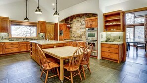 A spacious kitchen with wooden cabinets, a large island, and a dining area with chairs. - Post Oak Estate - Pool, Barn, 2 Guest Homes, 16 Ac (Cleburne)